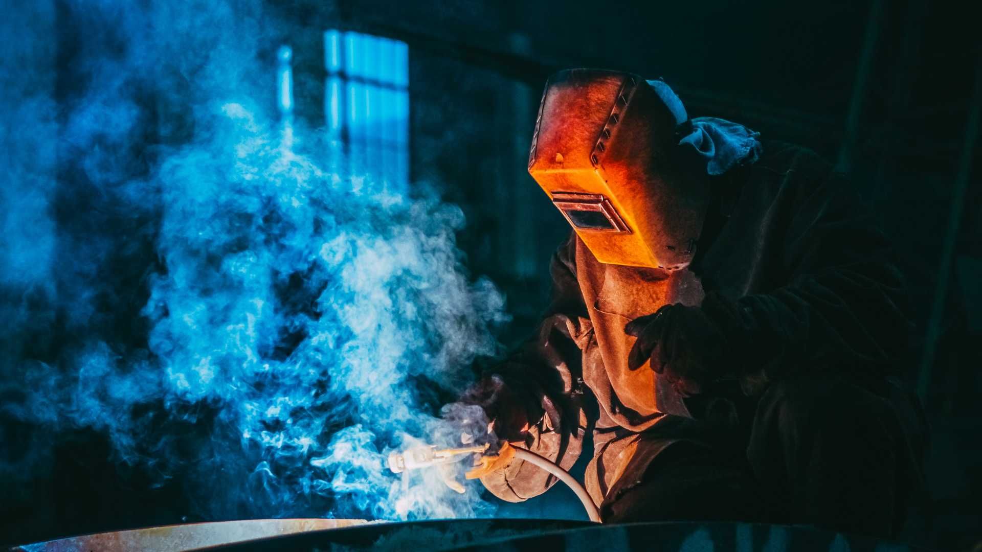 A man wearing a welding mask is welding a piece of metal.