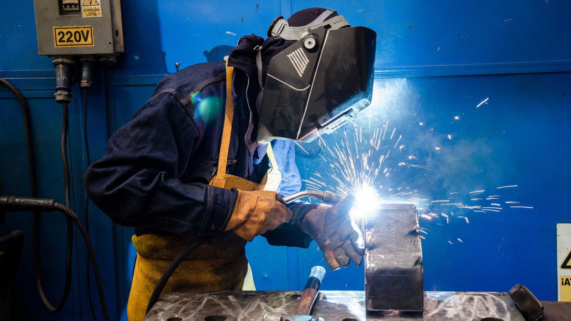 A man is welding a piece of metal in a factory.