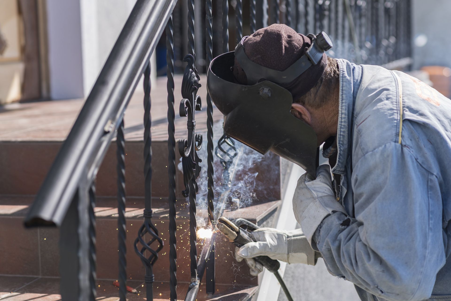 A man wearing a welding mask is welding a railing on a set of stairs.