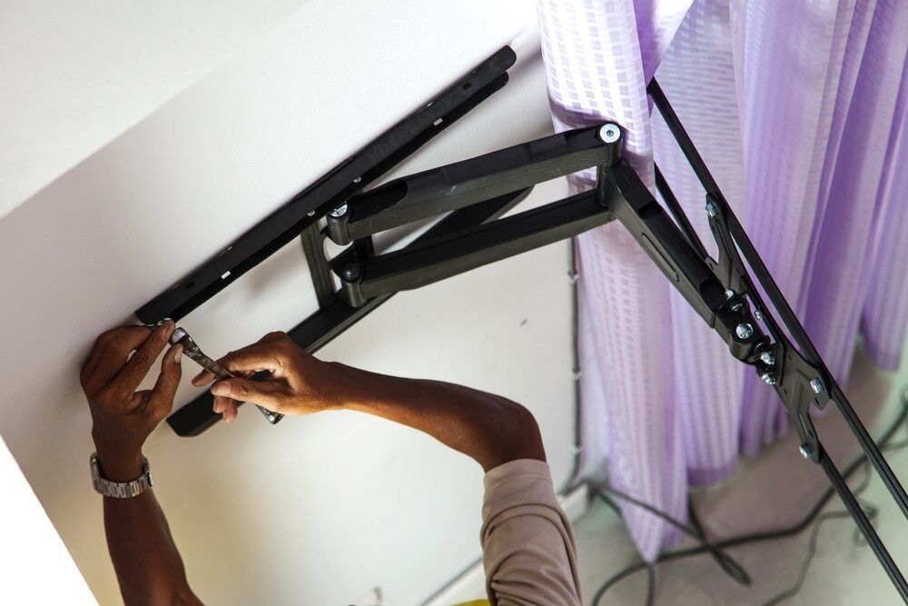 A Person Is Working On A Tv Mount With Curtains In The Background — Bradshaws Radio & TV Service In Maryborough, QLD