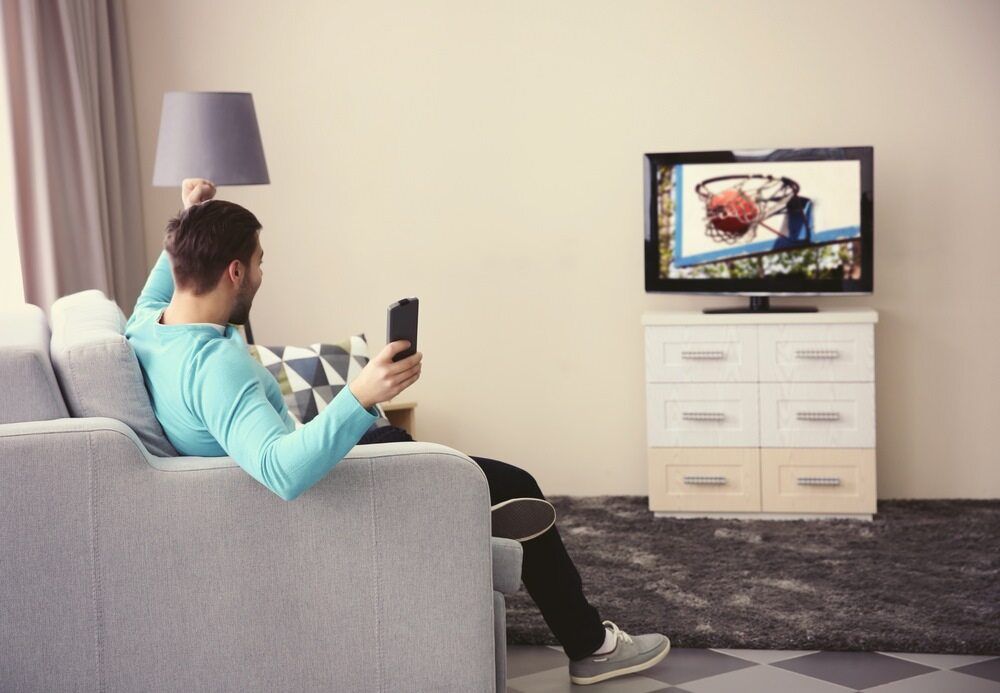 A Man Is Sitting On A Couch Watching On Television — Bradshaws Radio & TV Service In Maryborough, QLD