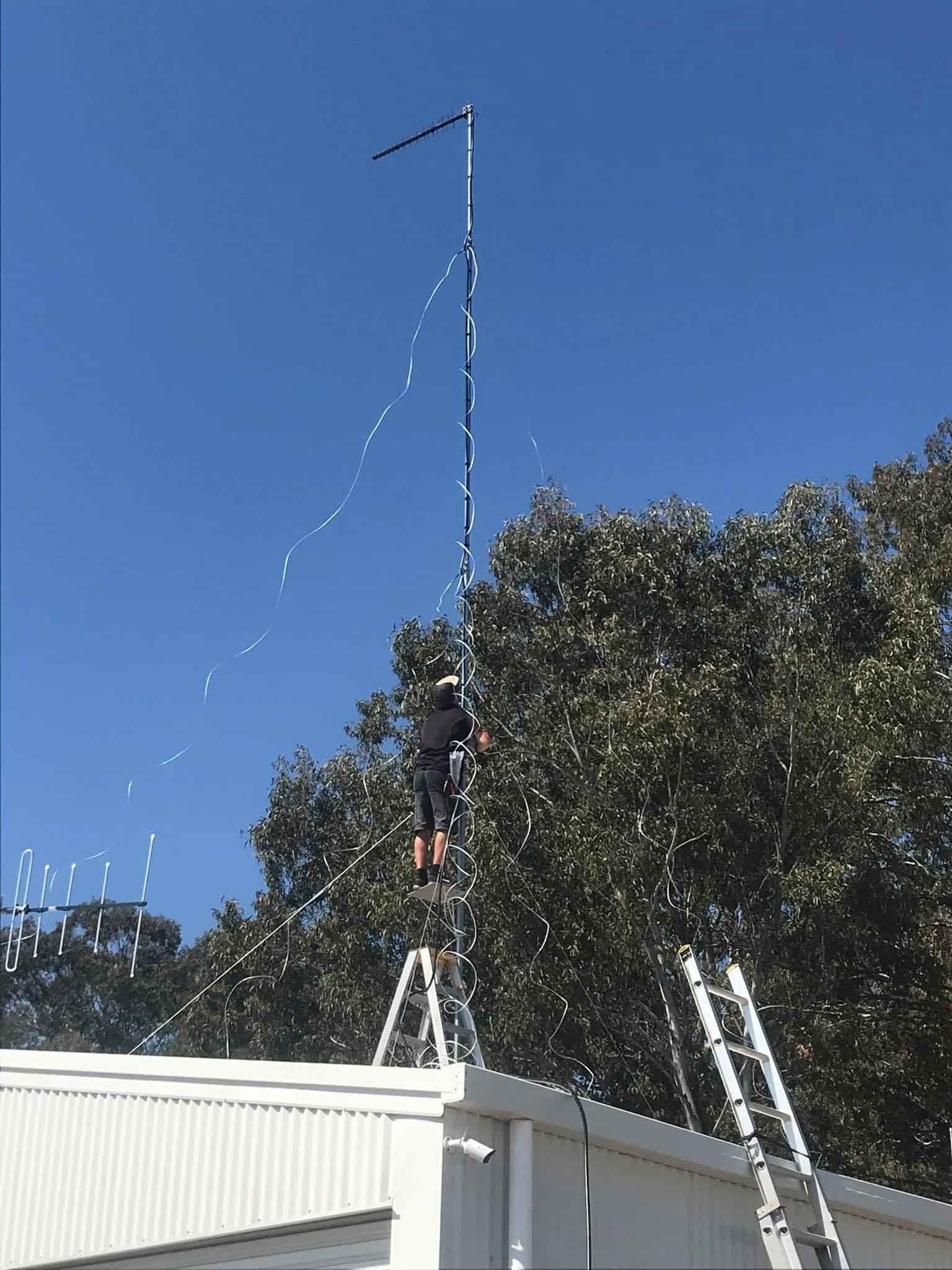 A Man Is Standing On A Ladder On Top Of A Building — Bradshaws Radio & TV Service In Maryborough, QLD