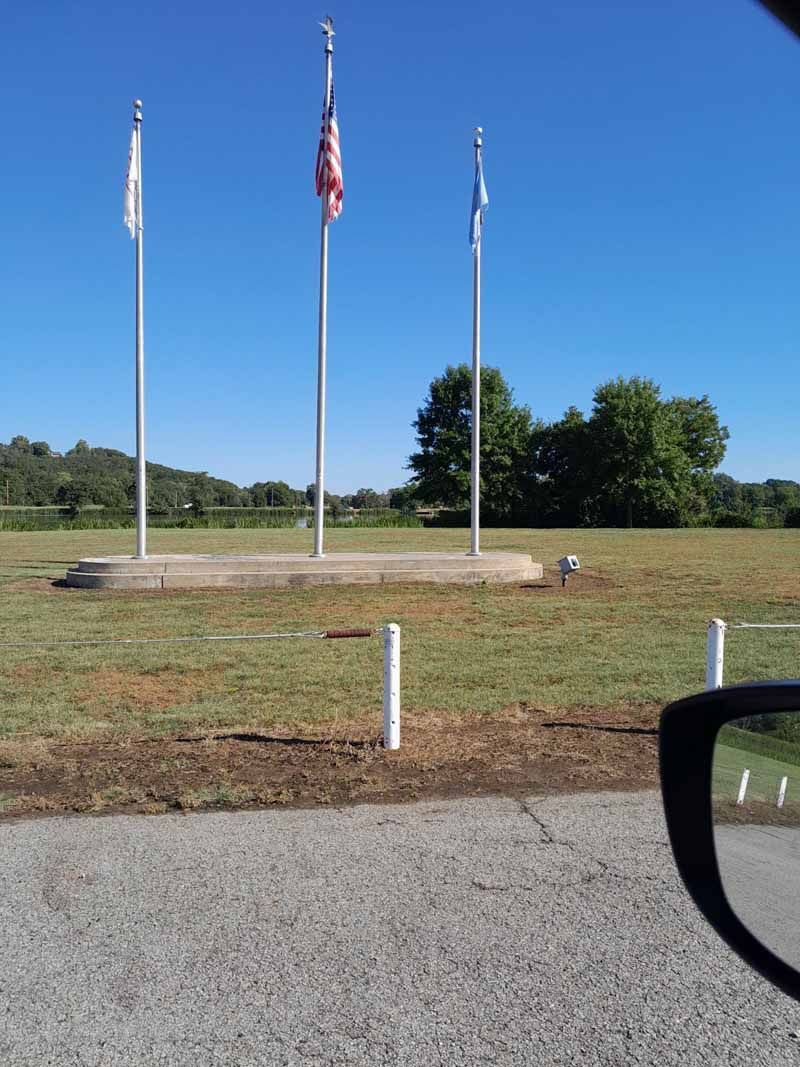 Three flags on poles in a grassy field; blue sky background.
