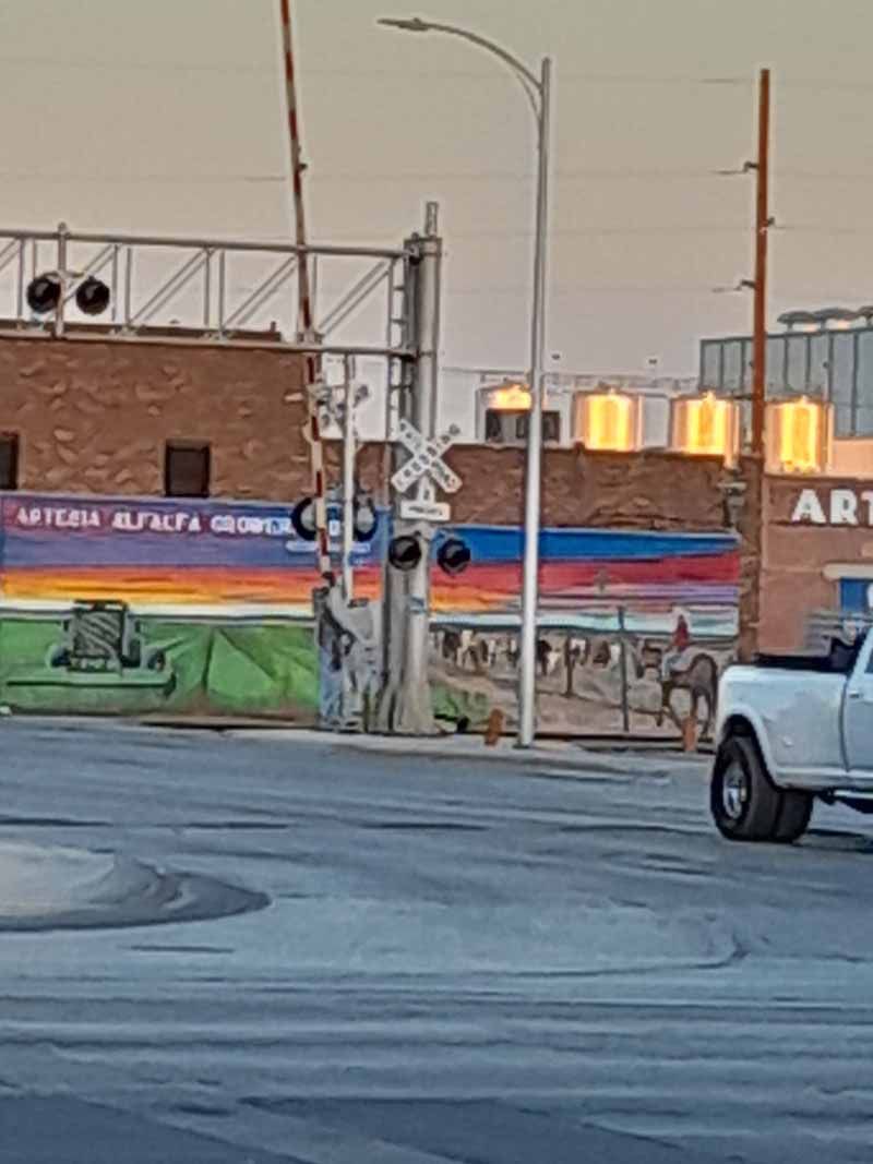 Railroad crossing with a mural, cowboy on a horse, and a truck. Sunset.