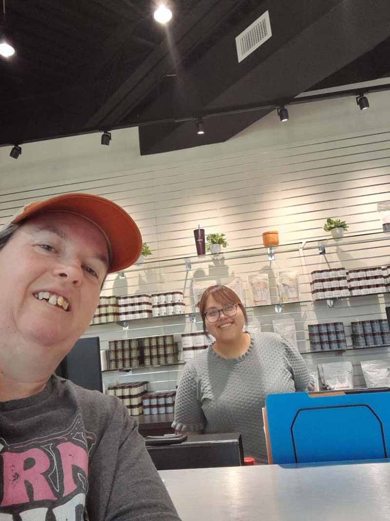 Two women at a store counter; one smiling, wearing an orange hat; the other smiling, at the register.