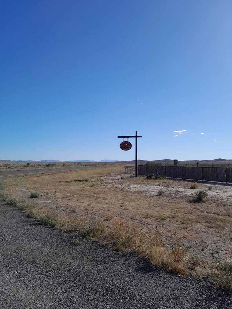 Signpost in a dry, open landscape under a bright blue sky, with sparse vegetation.