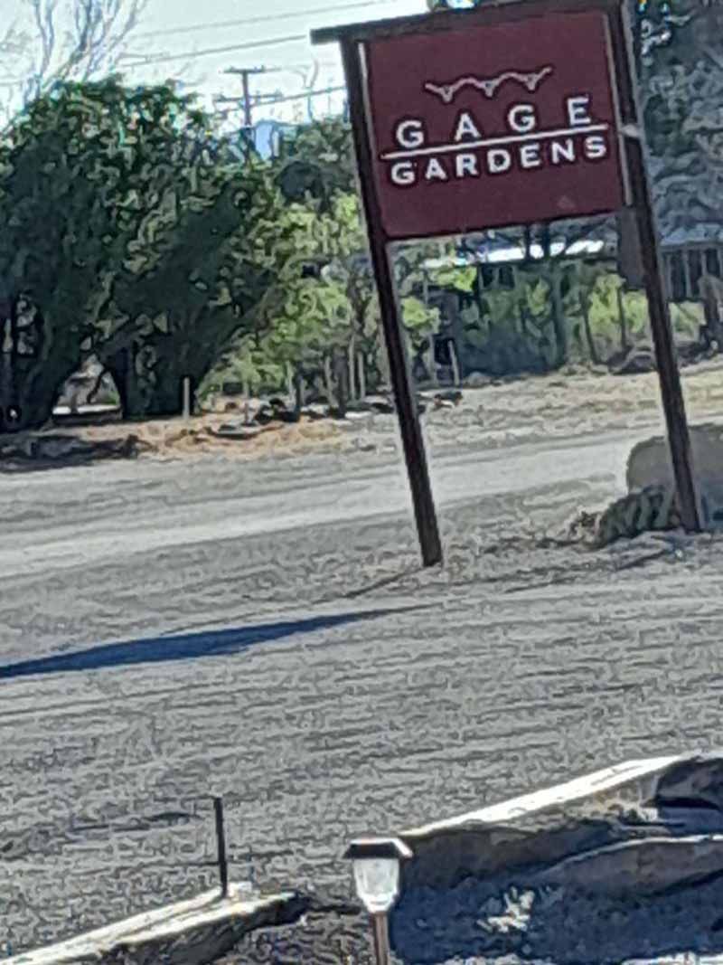 Sign for Gage Gardens on a gravel road. The sign is brown with white lettering.