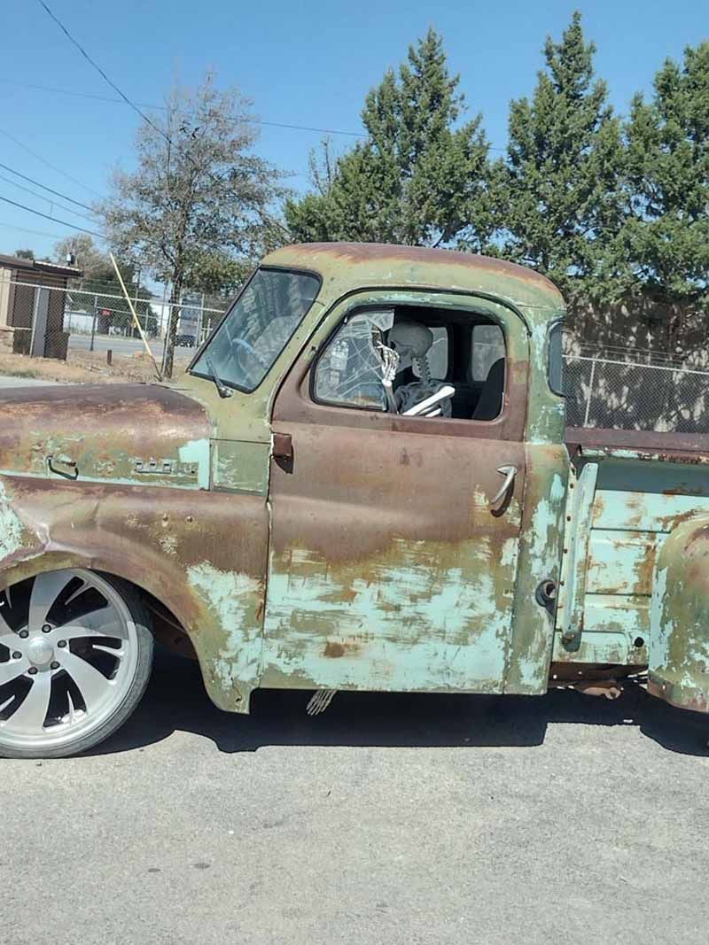 Rusty, low-rider vintage pickup truck with green paint and custom wheels parked on a paved road.