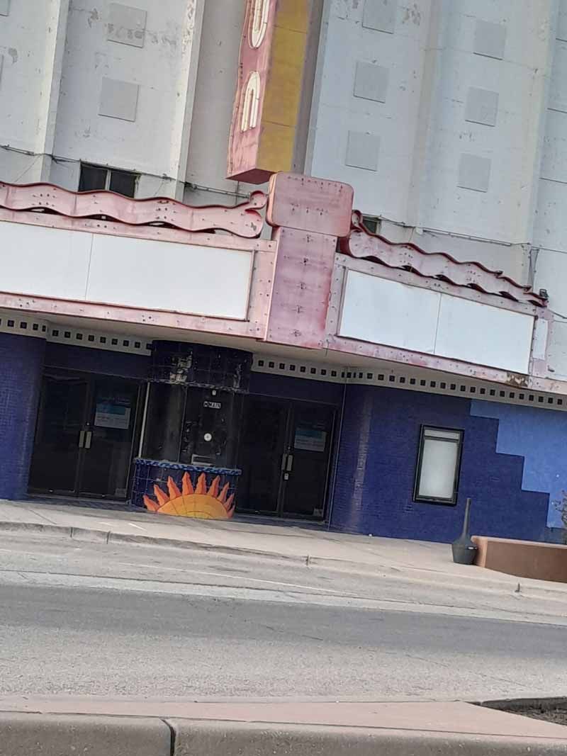 Exterior of a vintage theater with a blue facade, pink trim, and blank marquee.