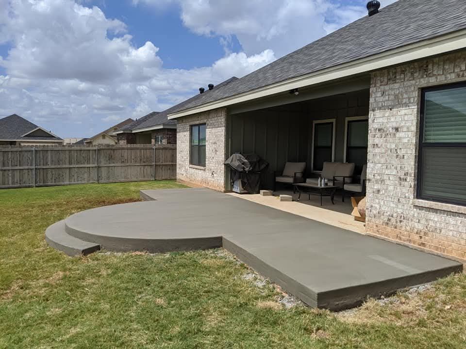 New concrete driveway in front of a brick house on a cloudy day. A truck and portable toilet are nearby.