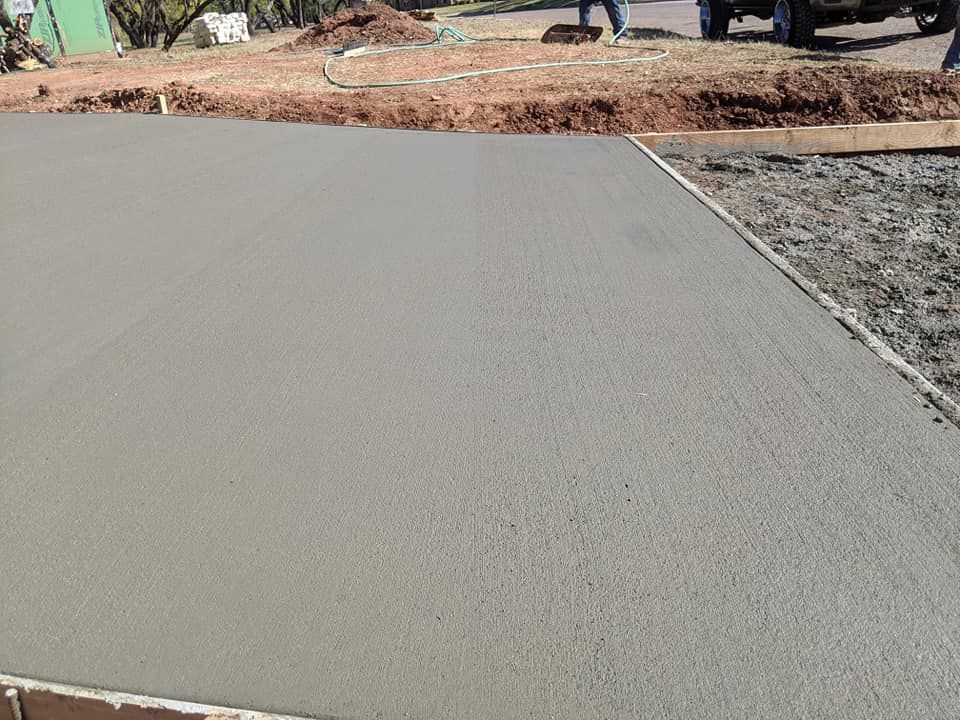 Freshly poured gray concrete surface. Construction site with dirt and tools.