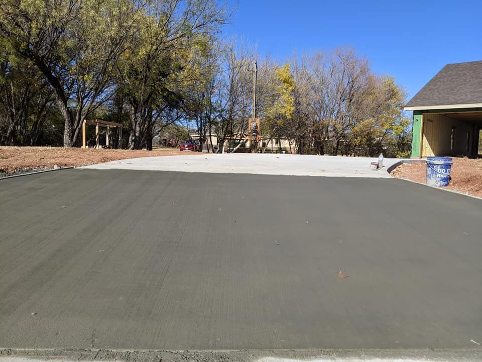 A freshly poured concrete driveway in front of a house under construction; trees in the background.
