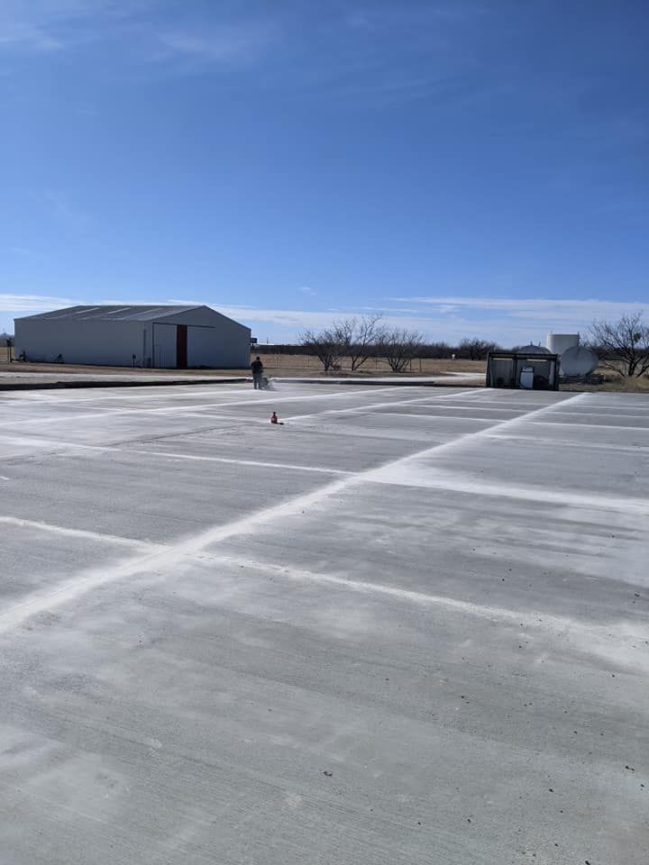 Man spraying white substance on a large concrete surface with a building and sky in the background.