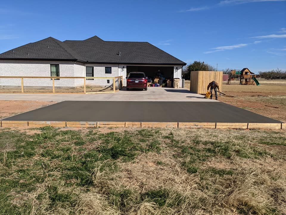Newly poured concrete driveway with wooden border in front of a house; a worker is smoothing the surface.
