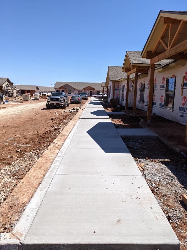 Construction site with new sidewalks and houses. Dirt, concrete, and blue sky.
