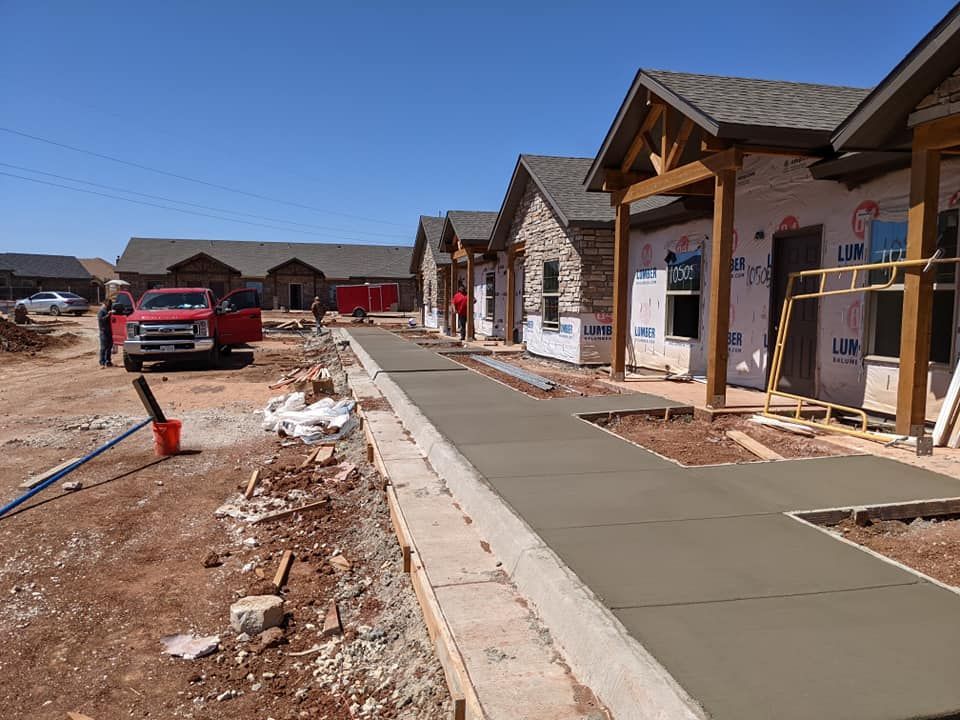Construction site with workers pouring concrete sidewalks near new buildings.