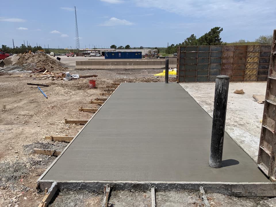 Newly poured concrete slab with two pipes, in a construction area, under a blue sky.