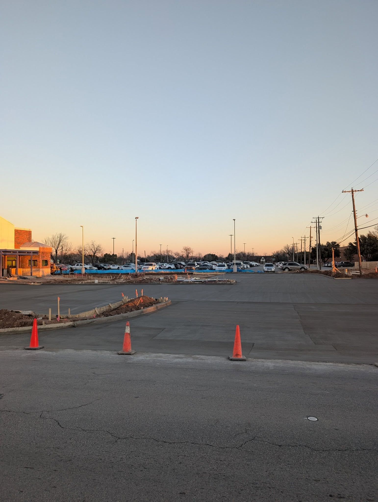Empty parking lot under a clear sky; construction cones mark new pavement.