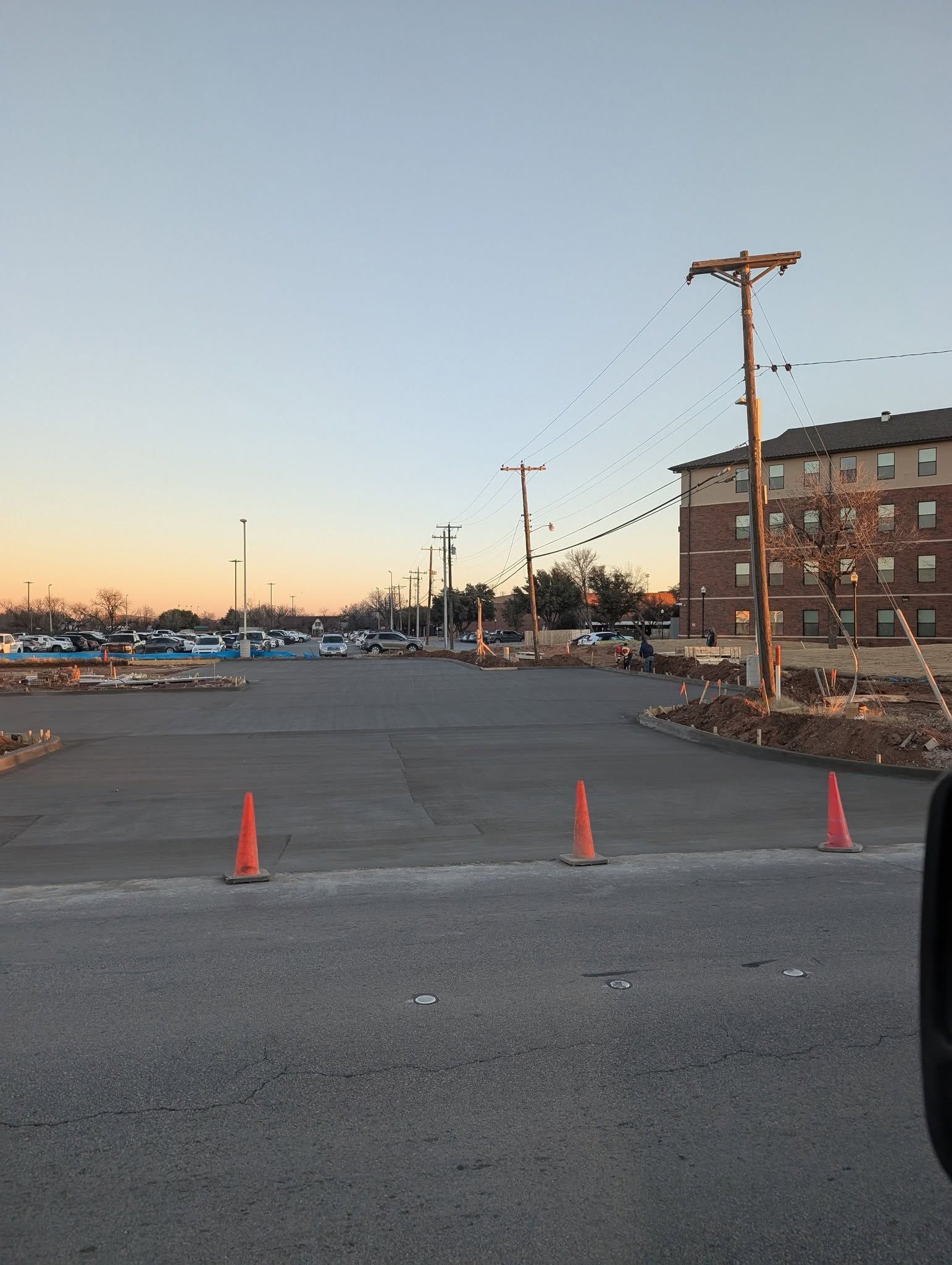 Construction zone in a parking lot with traffic cones, power lines, and a brick building.