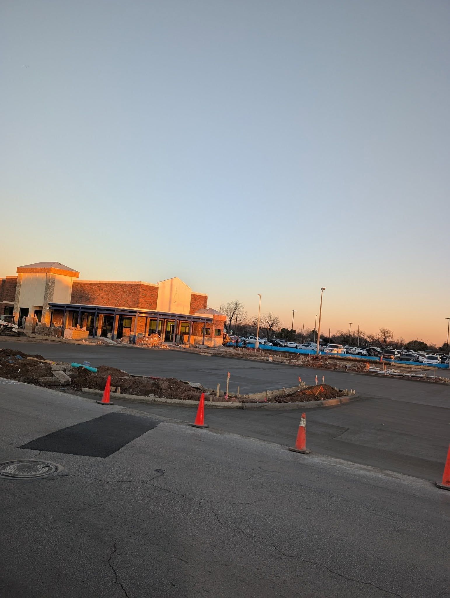 Restaurant under construction with orange cones, blue sky, and setting sun.