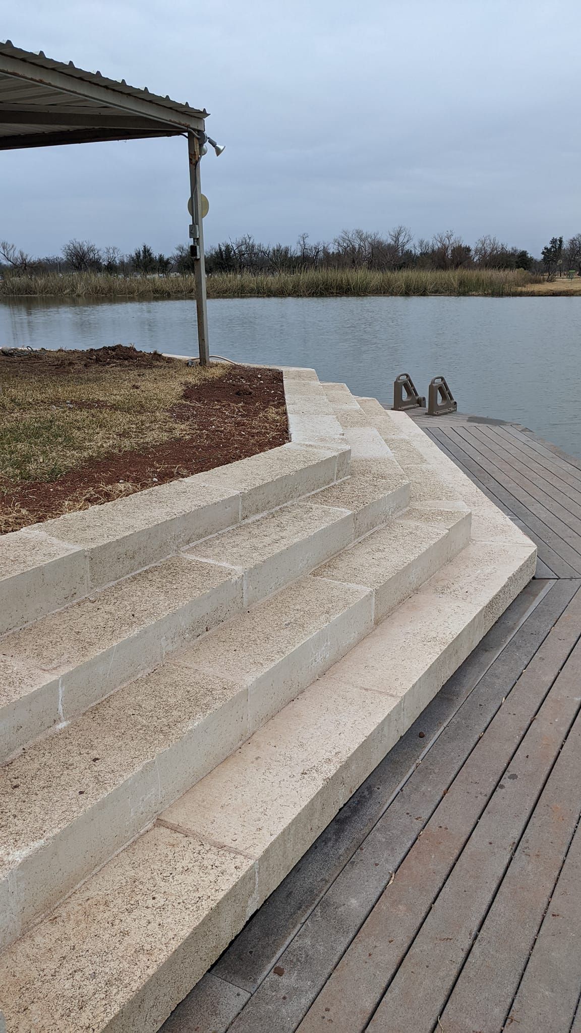 Stone steps leading into a body of water, next to a brick-paved walkway and grassy area, under an overcast sky.