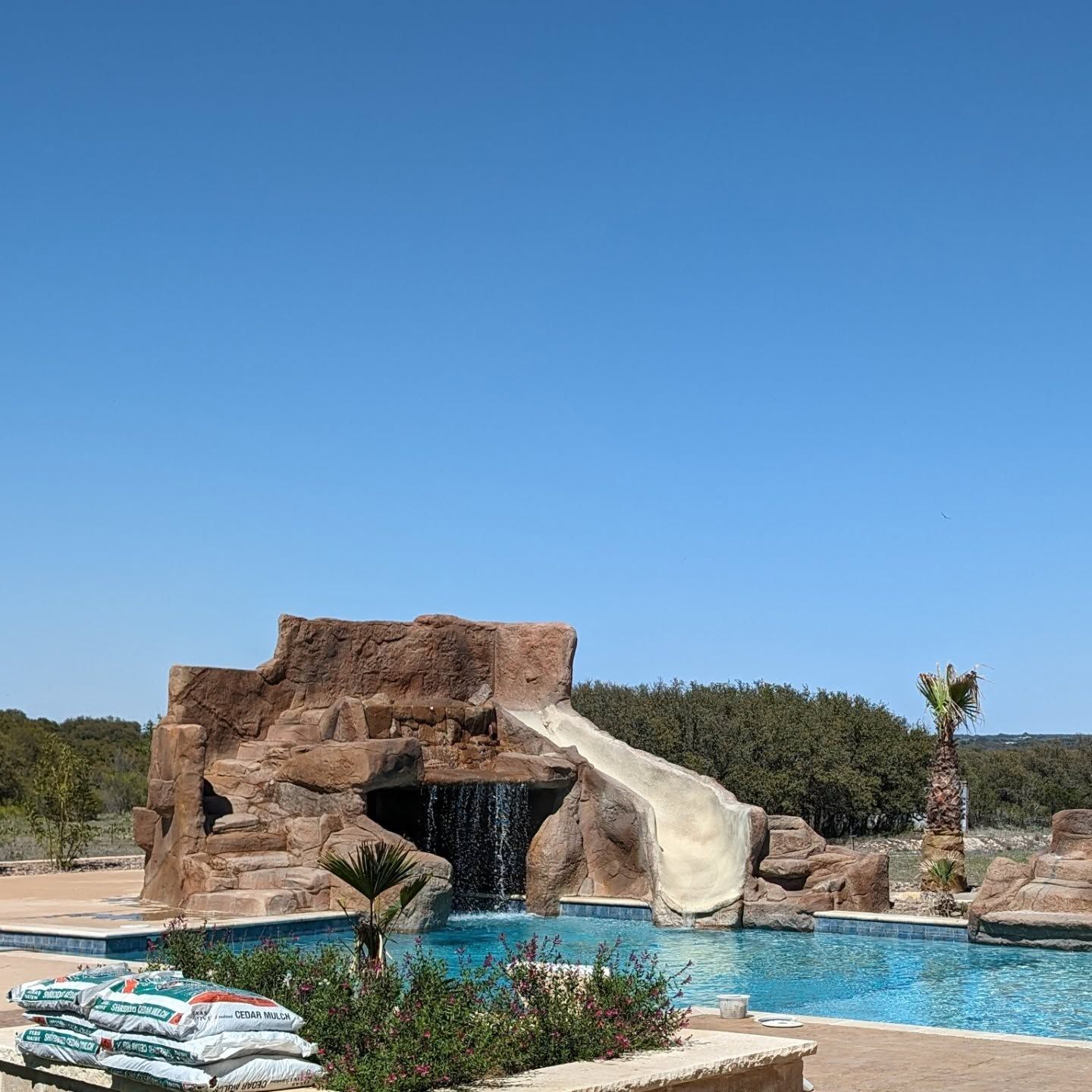Swimming pool with rock waterfall, slide, blue water, clear sky.
