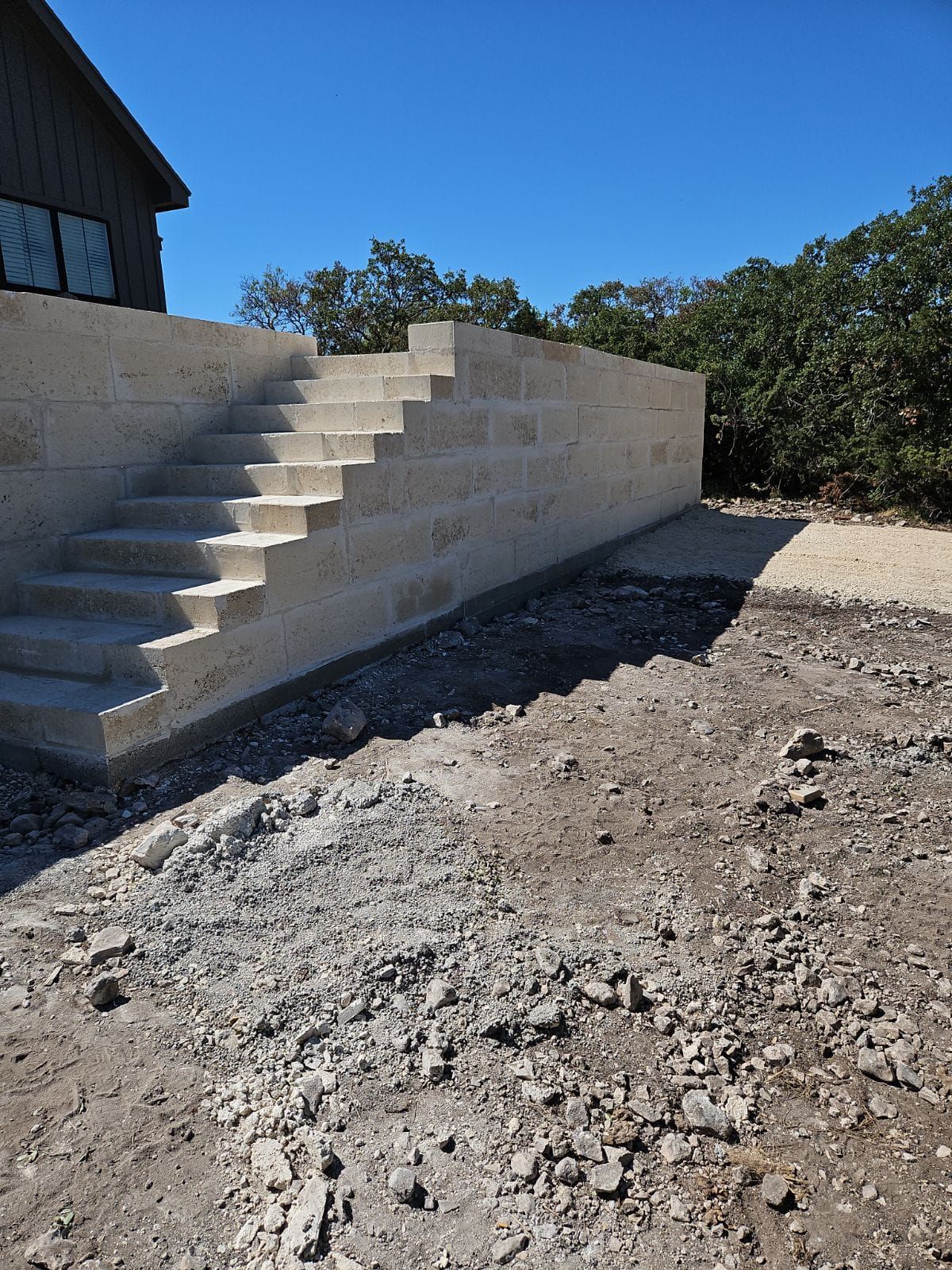 Concrete stairs and retaining wall in a dirt setting, leading to a house under construction.