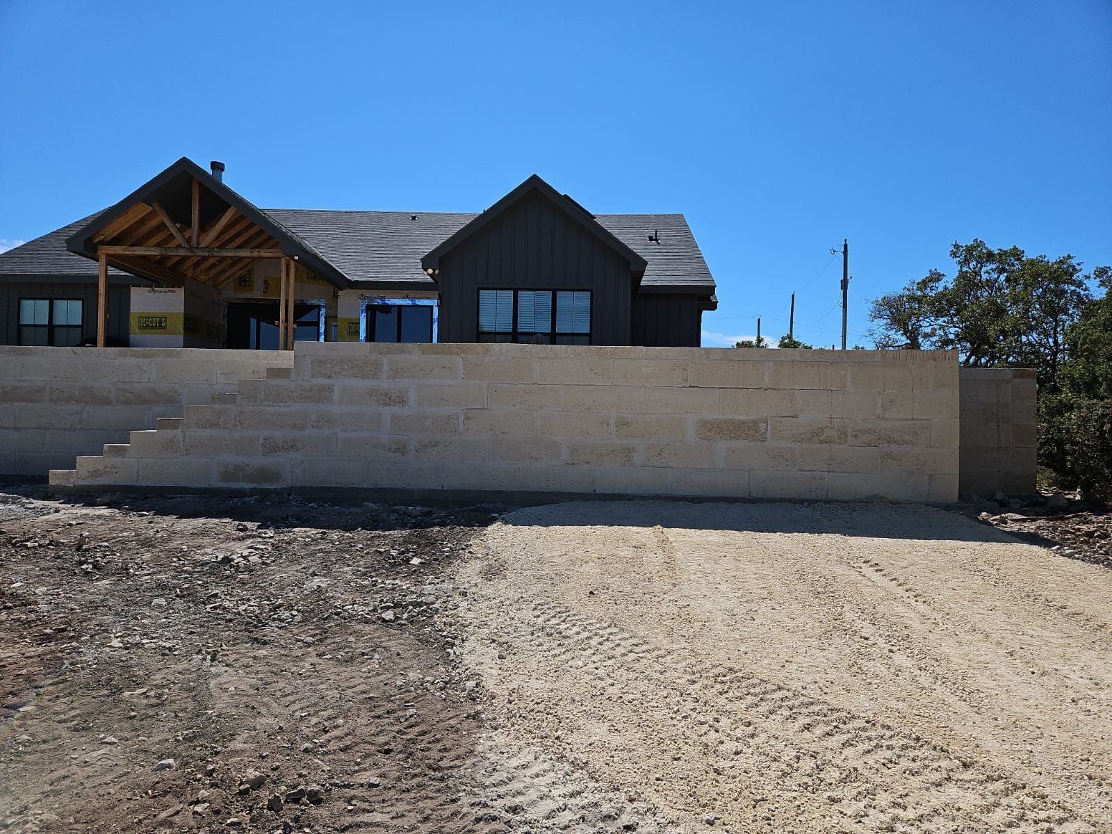 Exterior view of a house with retaining wall and gravel driveway under a blue sky.