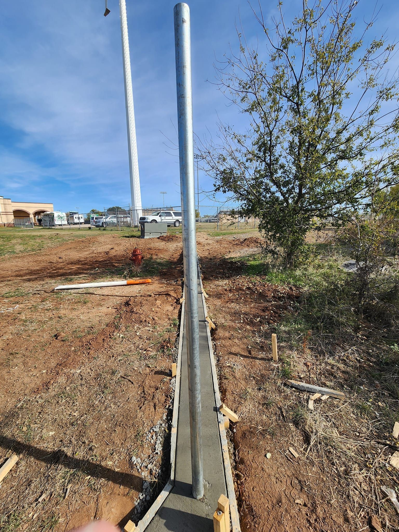 A tall, metal pole is set in a concrete foundation. Construction site, outdoor, sunny day.