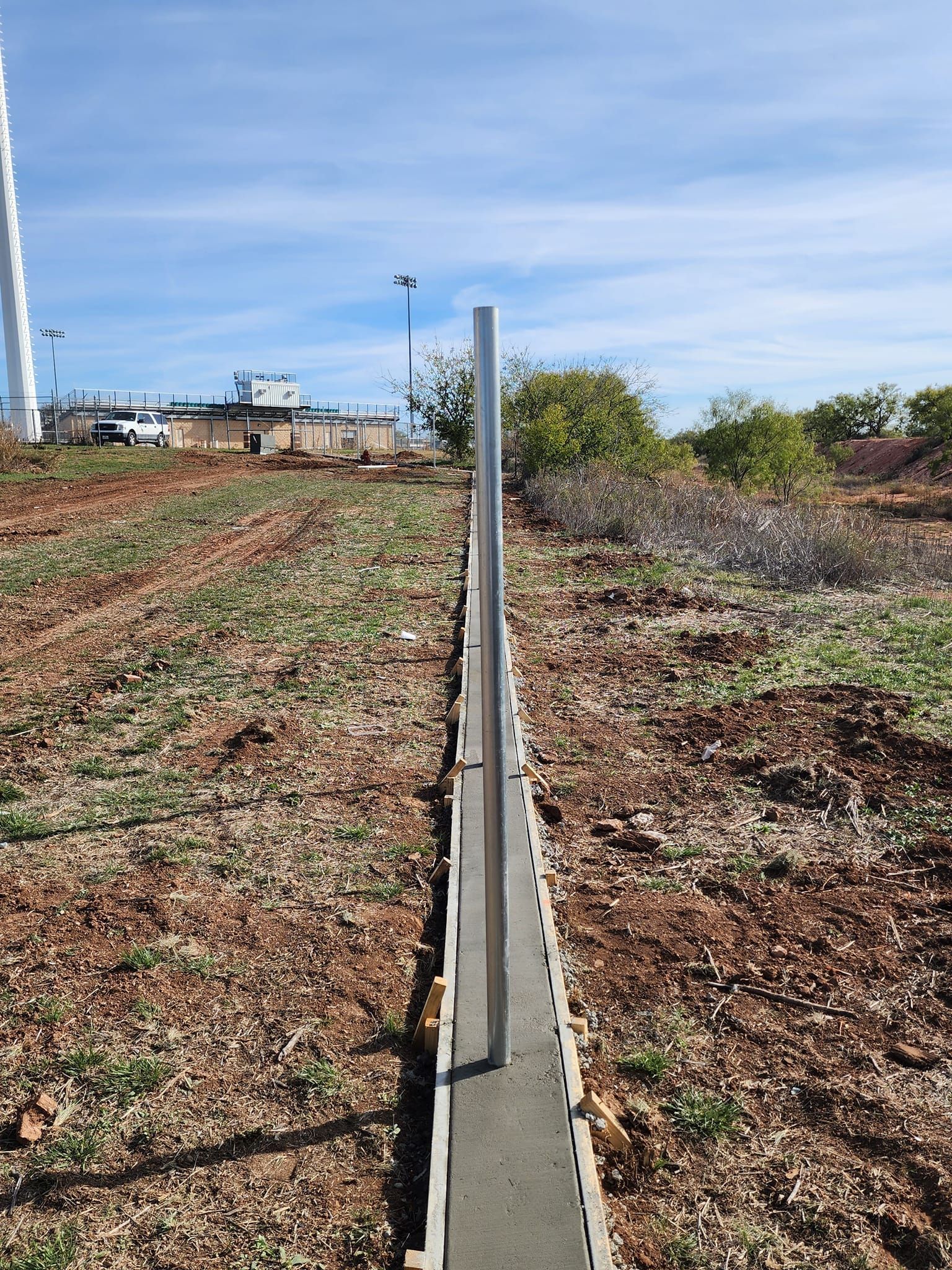 Concrete form with a metal post set in fresh concrete, outdoors.