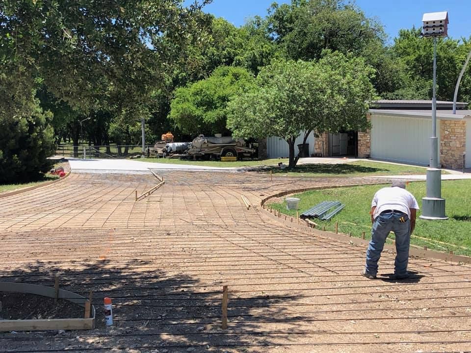 Construction worker on concrete work site, placing rebar. Outdoors with trees and building in the background.