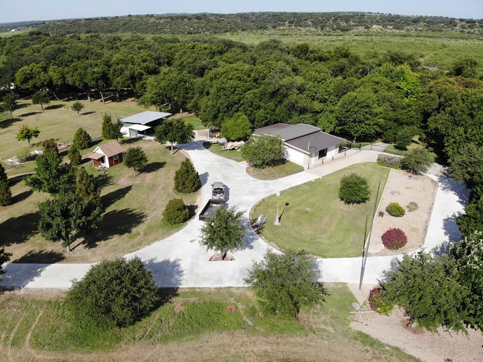 Aerial view of a property with buildings, driveway, and surrounding trees.