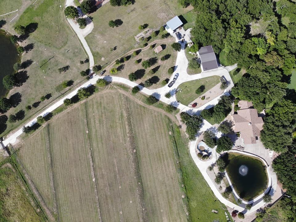 Aerial view of a rural property with a house, pond, fields, trees, and long driveway.