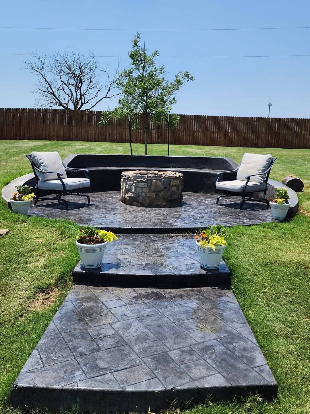 Patio with concrete pathway, fire pit, seating, and potted plants on a sunny day.