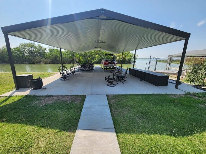 Covered outdoor area with exercise equipment, overlooking water. Green grass in foreground.