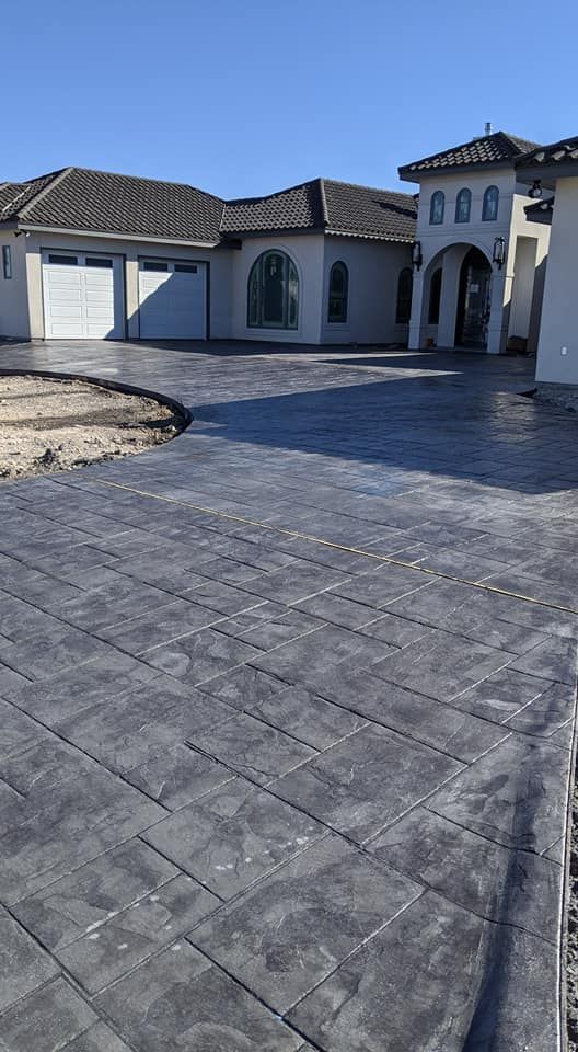 Brick-patterned concrete driveway leading to a light-colored stucco house with a two-car garage on a sunny day.