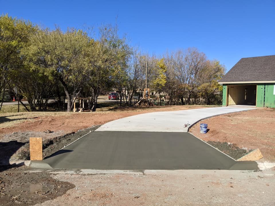 Concrete driveway under construction leading to a house, with green siding and a gravel yard.