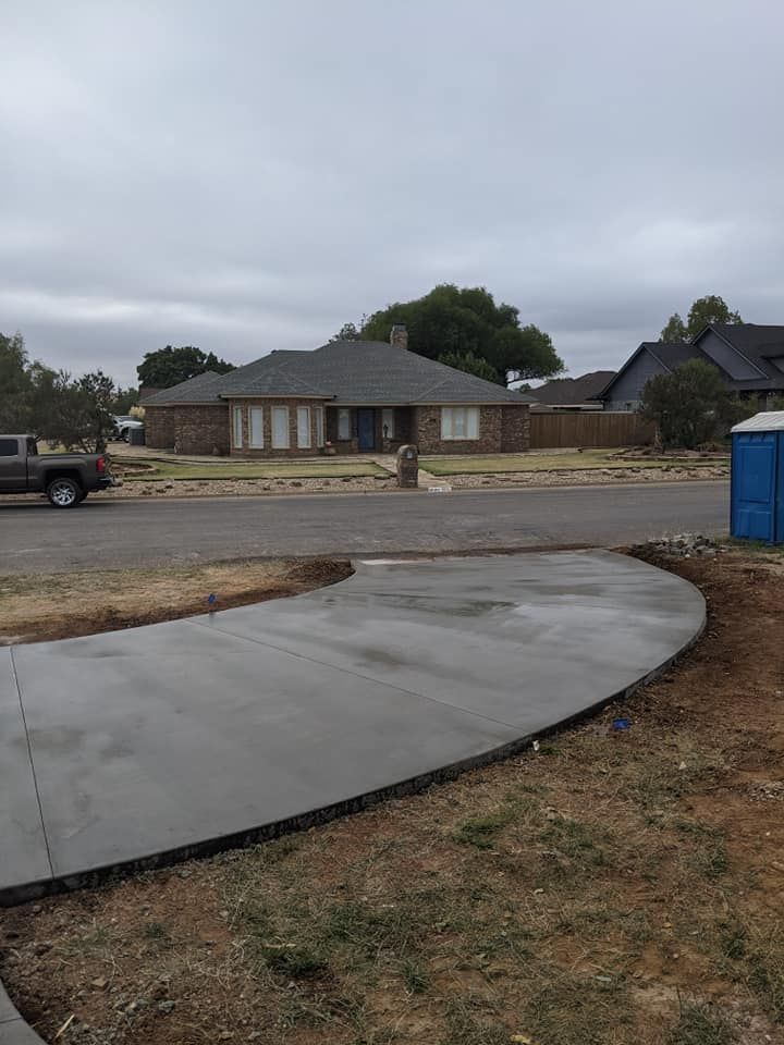 A newly poured concrete driveway curves in front of a house on a cloudy day.