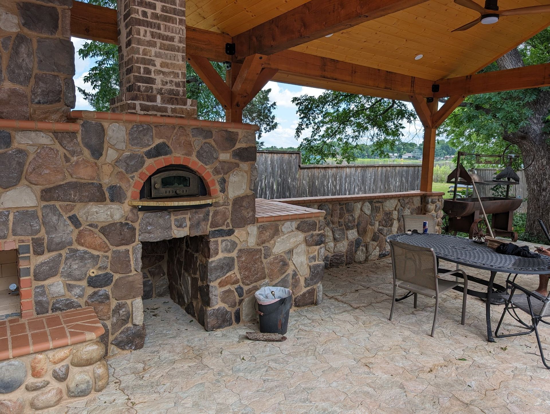 Outdoor kitchen with stone oven and grilling area under a wooden pergola.