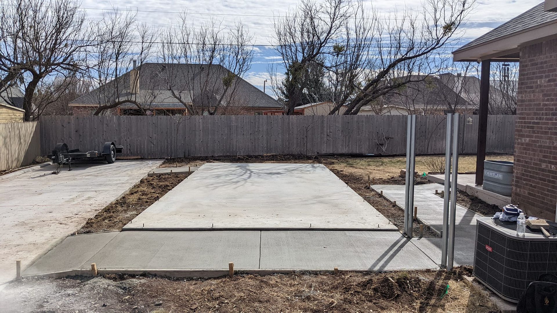 Backyard with new concrete pad. Wooden fence in background. Brick house on the right.
