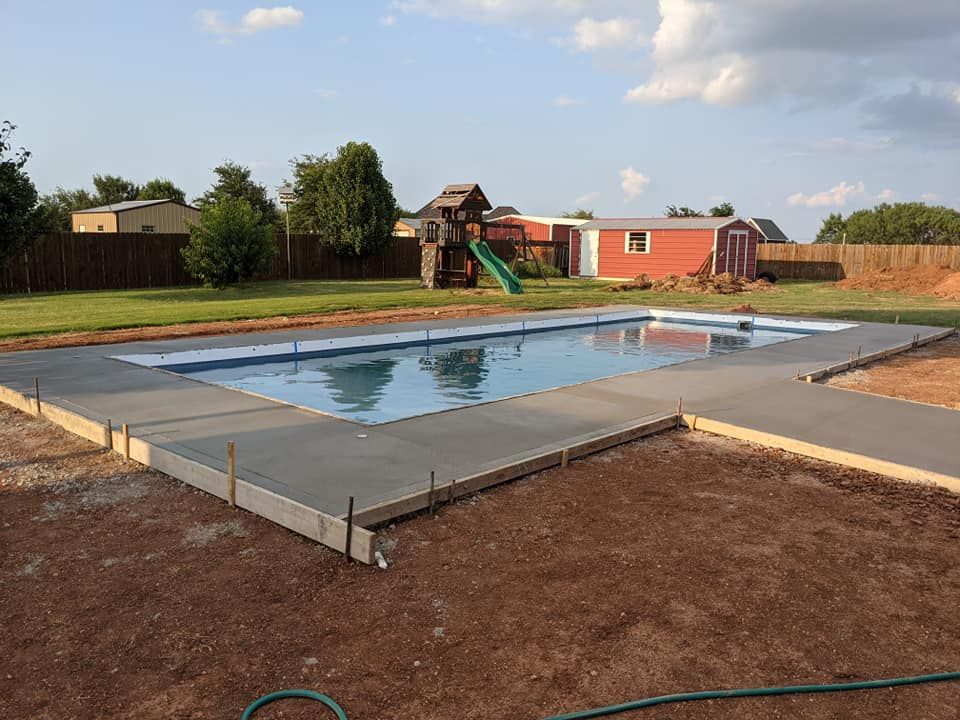 Swimming pool with concrete border in a backyard. Red playhouse and shed in background.