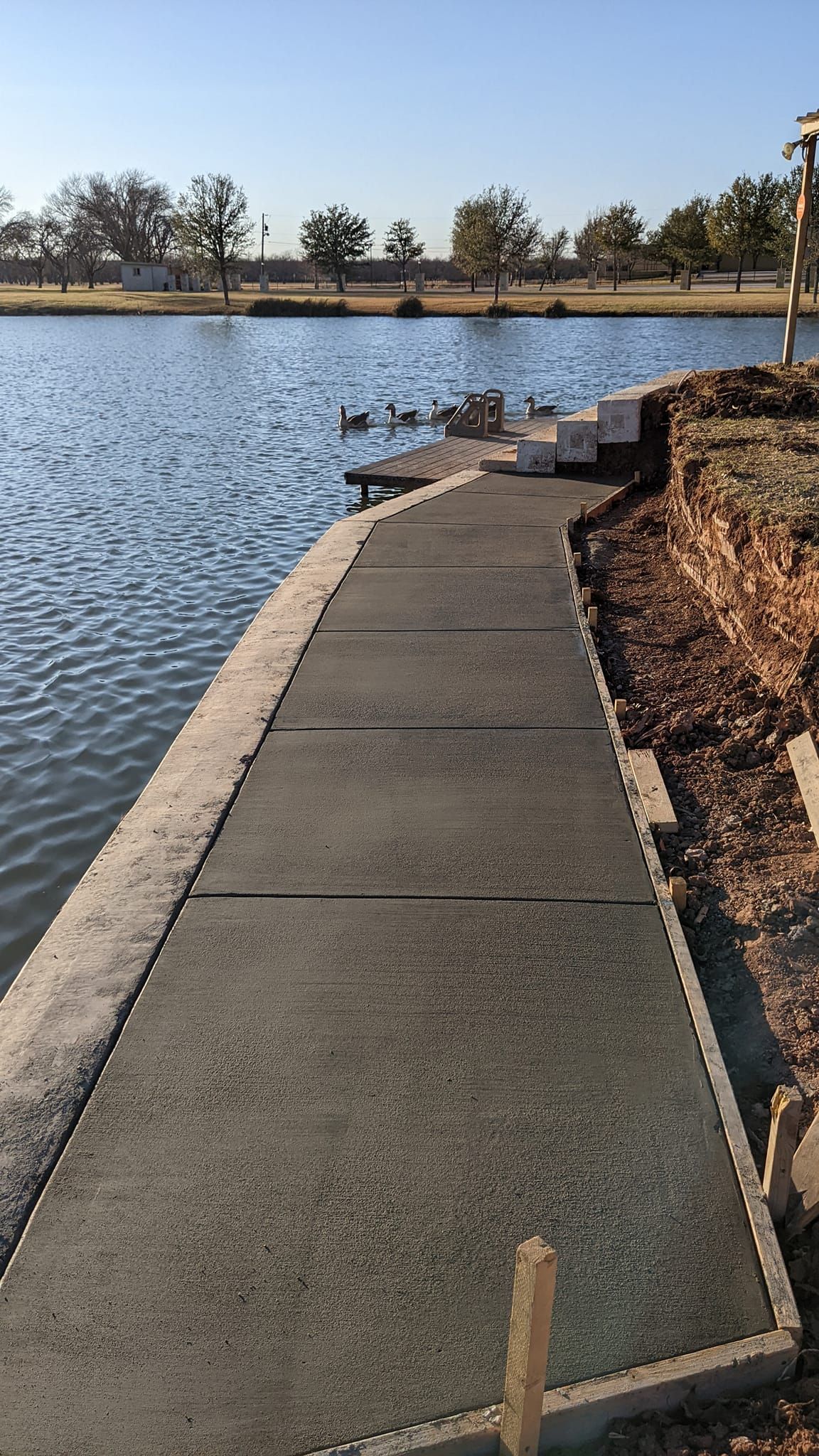 A newly constructed concrete path along a lake's edge.