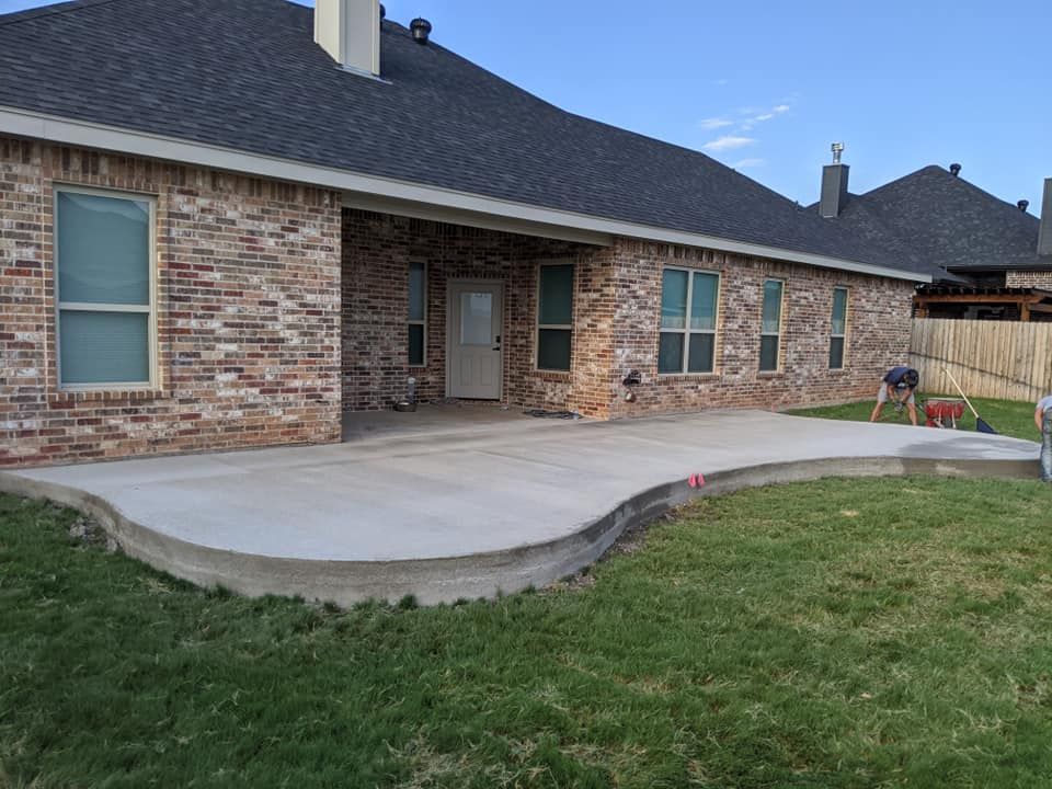 A new concrete patio curves away from a brick house. Green grass surrounds it.