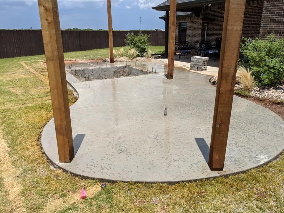 Newly poured concrete patio with wooden support beams in a backyard.