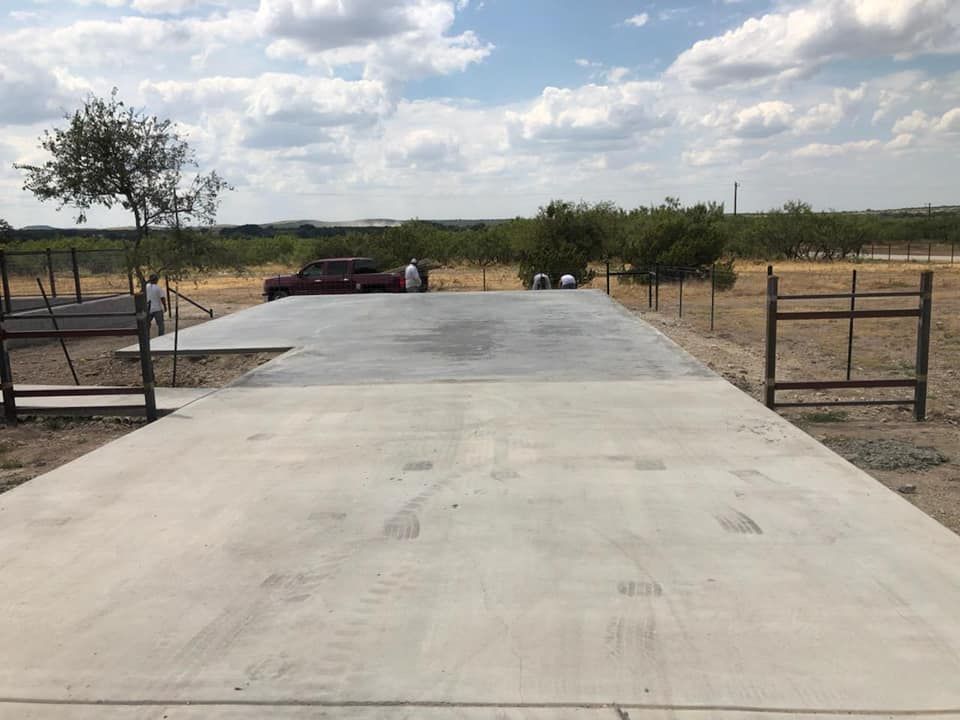 A large concrete pad in an open field, with a vehicle and trees in the distance under a cloudy sky.