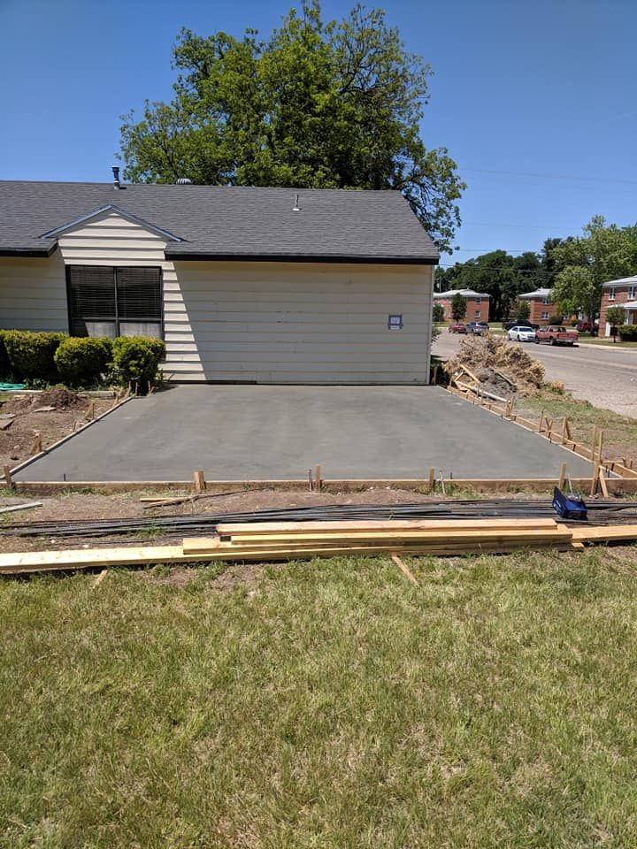 New concrete driveway in front of a beige building, surrounded by wooden framing, grass, and a sunny day.