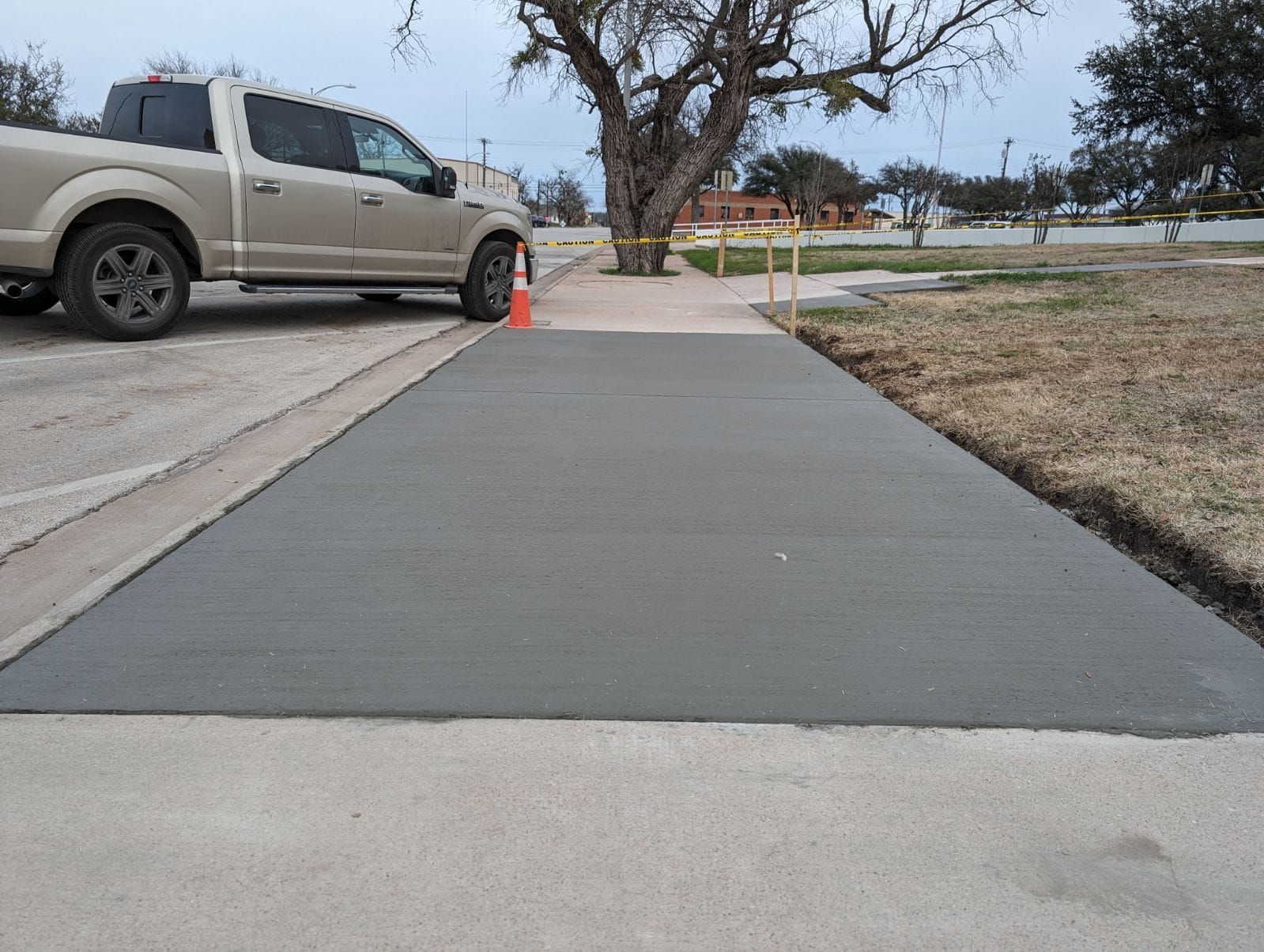 Freshly poured gray concrete sidewalk next to a beige pickup truck and a grassy area.