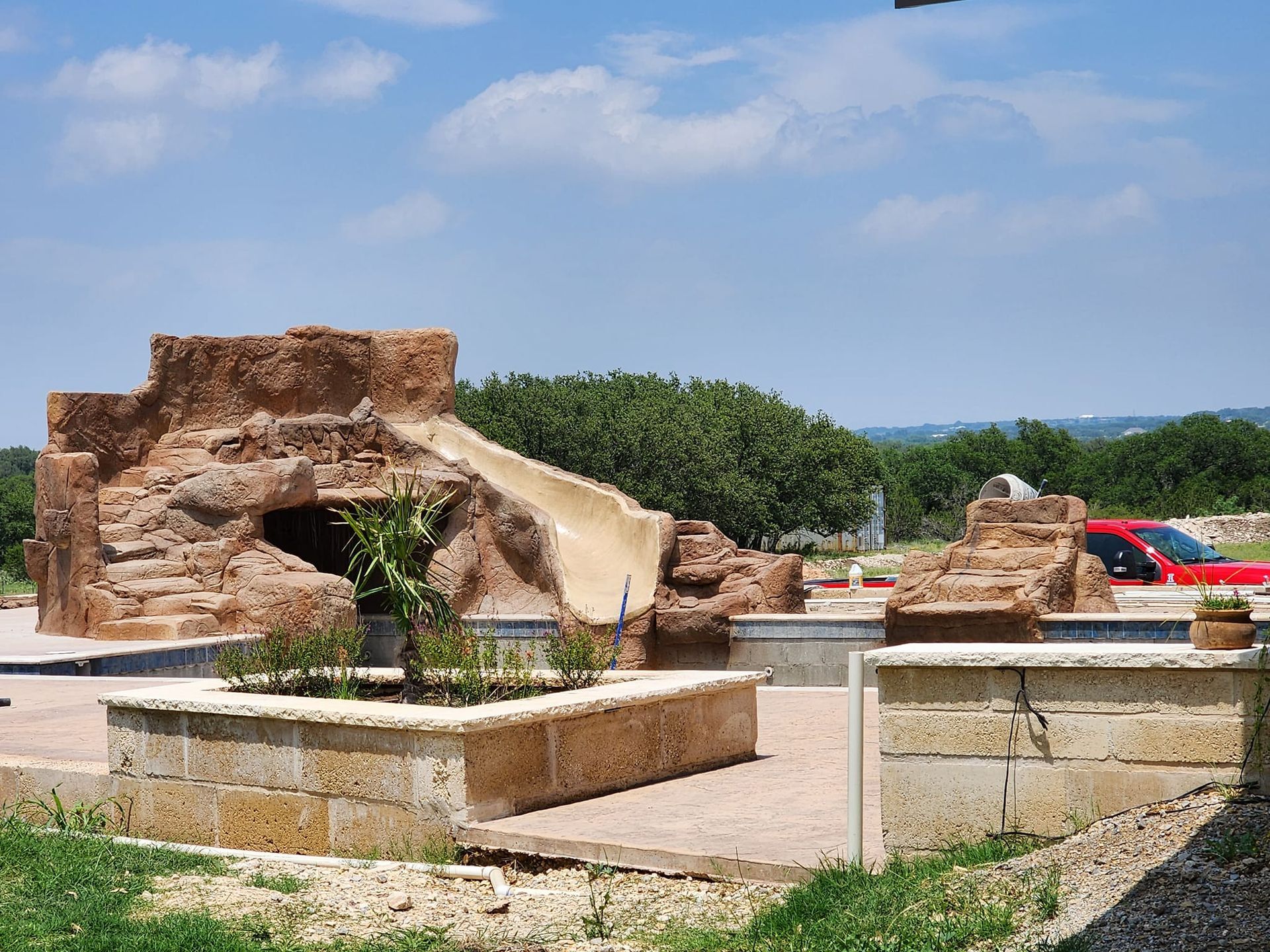 Playground with stone walls, brown slide, and red car in the background.