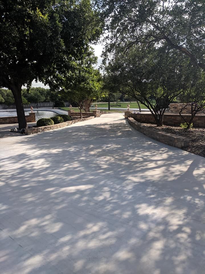 Concrete path through a park, flanked by trees casting shadows.