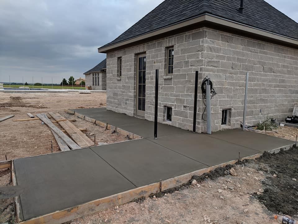 Newly poured concrete walkway next to a stone building under construction.